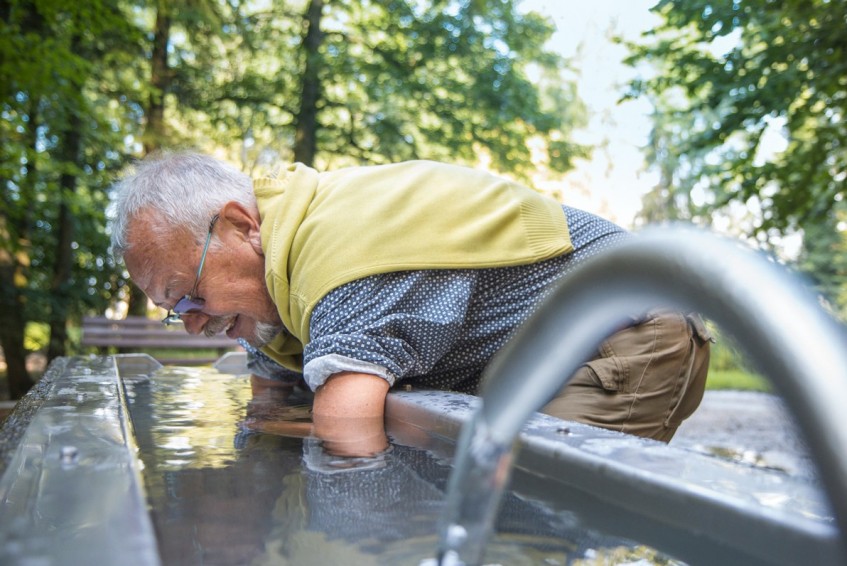 Ein älterer Mann taucht seine Arme in ein öffentliches Wasserbecken.