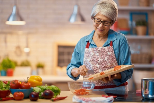 Eine etwa 60-Jährige schiebt geschnittene Tomaten vom Brett in eine Salatschüssel.