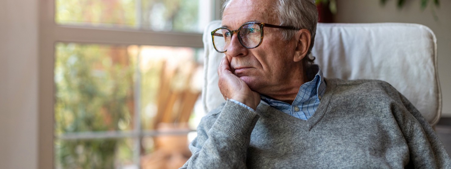 Ein etwa 70-jähriger Mann sitzt mit dem Kopf in die Hand gestützt im Sessel und blickt aus dem Fenster.