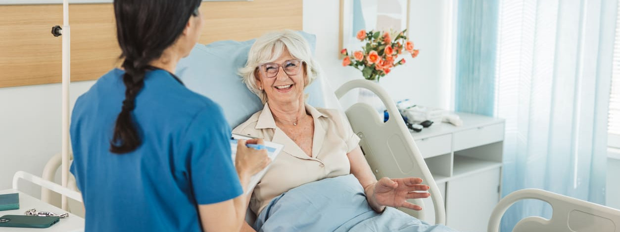 Krankenschwester begrüßt freudige ältere Patientin, die im Krankenbett liegt