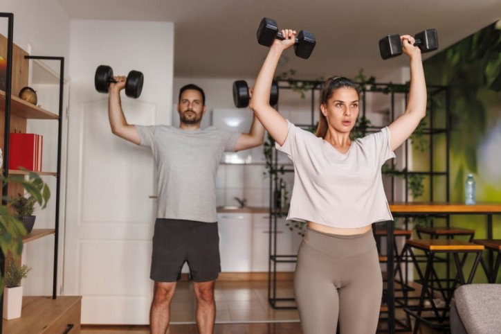 Ein Paar macht gemeinsam Krafttraining zuhause mit Hanteln