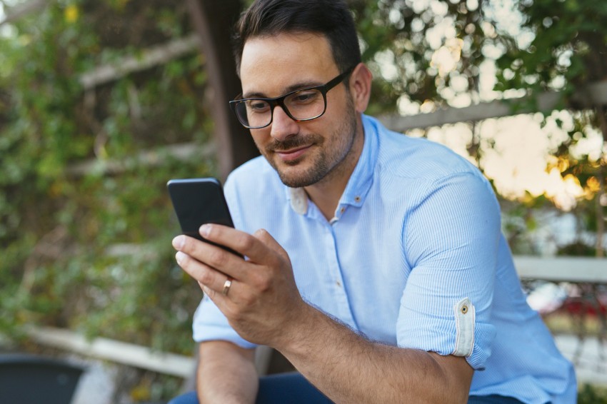 Ein etwa 40 jähriger Mann sitzt im Garten und schaut auf sein Smartphone. 