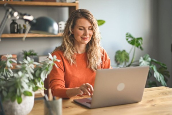 Eine etwa 40 jährige Frau sitzt am Tisch und schaut auf einen Laptop.
