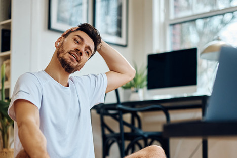 Ein etwas 35-jähriger Mann macht Nackenübungen auf seiner Matte zuhause.