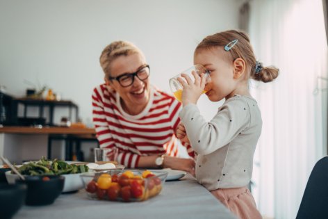 Mutter mit ihrer kleinen Tochter am Essenstisch, Tochter trinkt Orangensaft