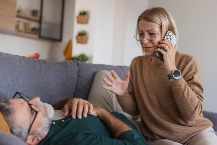 Eine ältere Frau wählt den Notruf für ihren ohnmächtigen Mann