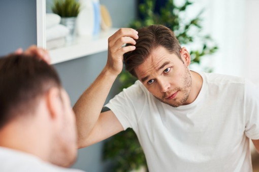 Ein etwa 30-jähriger Mann kontrolliert seinen Haaransatz im Spiegel.