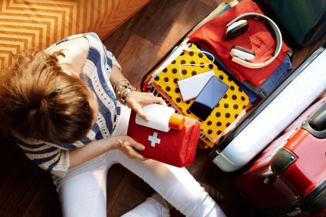 Eine junge Frau packt in einen Koffer ihre Reiseapotheke ein.