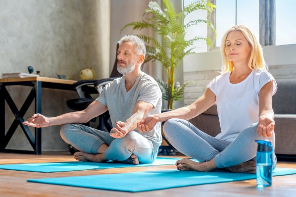 Ein etwa 60-jähriger Mann und eine 50-jährige Frau meditieren auf einer Yogamatte.
