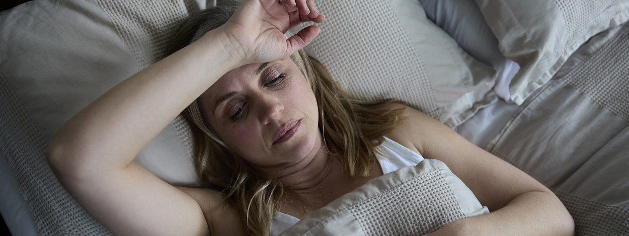 Eine etwa 40 Jahre alte Frau liegt erschöpft im bett. Ihre hand liegt auf ihrer Stirn