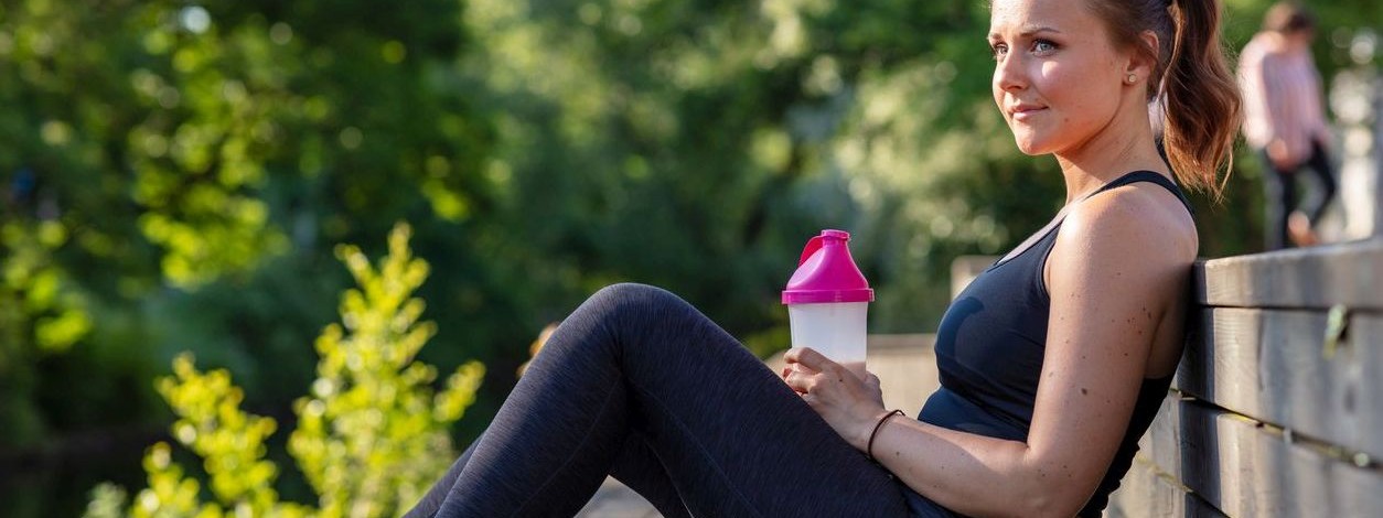 Junge Frau Anfang 20 trinkt nach dem Joggen einen Eiweißshake
