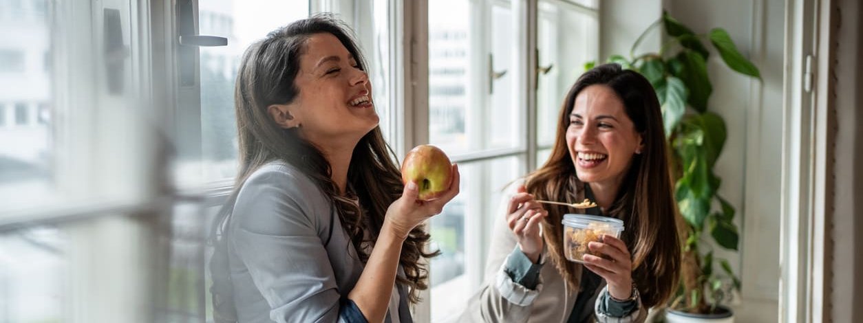 Zwei gute gelaunte Frauen nehmen in ihrer Mittagspause gesundes Essen zu sich
