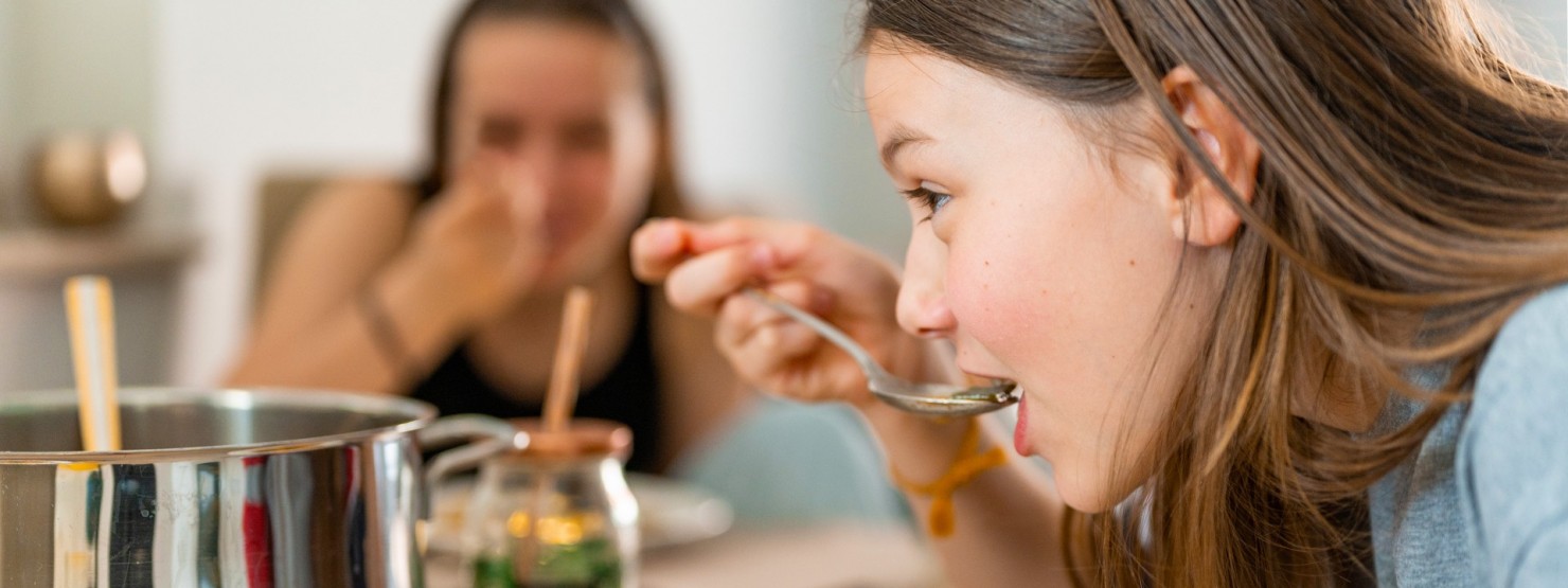 Zwei etwa 13-jährige Mädchen essen Suppe an einem Esstisch.