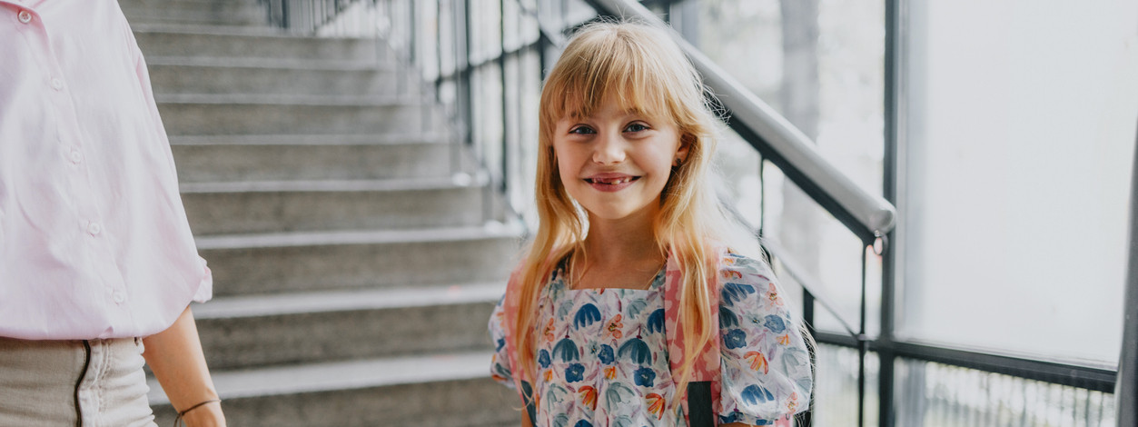 Mädchen mit Schulranzen vor Treppe im Schulgebäude