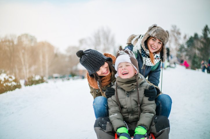 2 Frauen in Winterkleidung mit einem kleinen Jungen auf einem Schlitten im Schnee