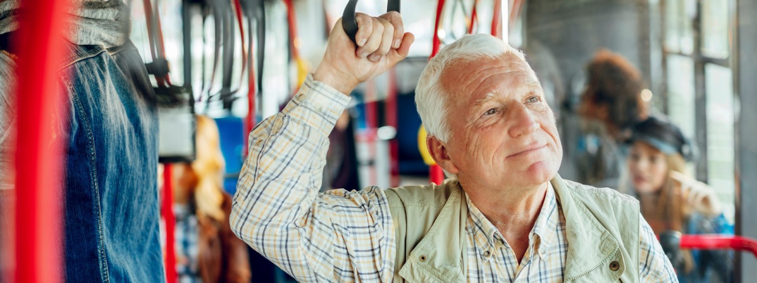 Ein etwa 70-jähriger Mann hält sich in einer Straßenbahn an einer Halteschlaufe fest.