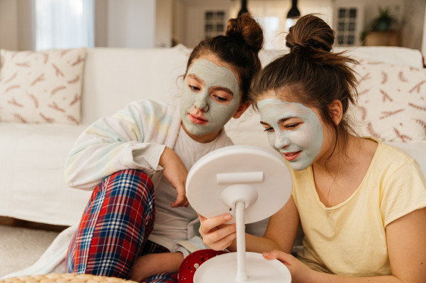 Zwei jugendliche Mädchen mit einer Beauty-Gesichtsmaske im Wohnzimmer.