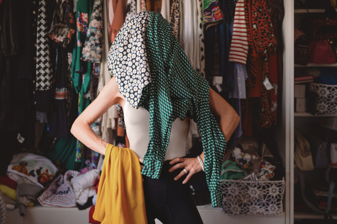 Eine junge Frau steht selbstbewusst posend mit Kleidern überm Kopf in einem üppig ausgestatteten Kleiderschrank. - AOK Sachsen-Anhalt begleitet mit starken Leistungen. 