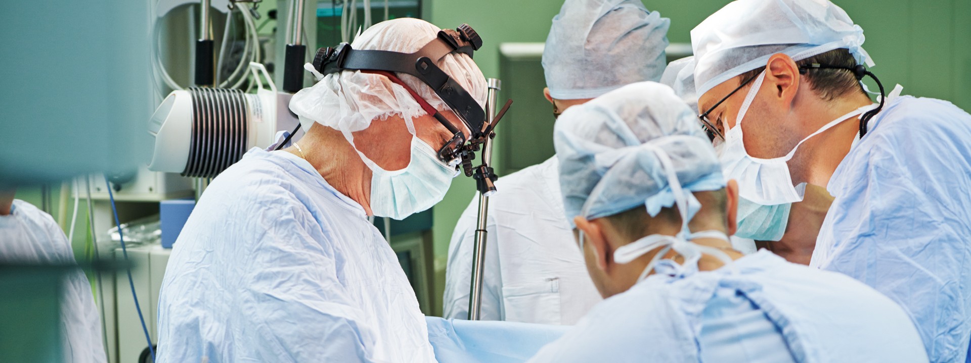 Mehrere Ärzte stehen mit OP-Kitteln in einem Operationssaal und operieren einen Patienten.