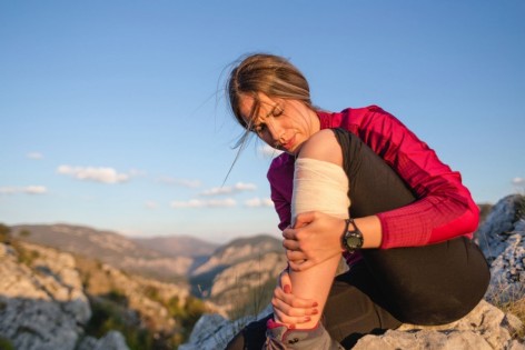 Eine etwa 30-jährige Frau sitzt auf einem Berg und hält ihr verletztes Bein still. 