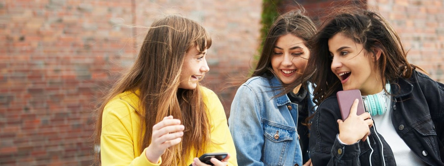 Drei etwa 16 jährige Mädchen sitzen zusammen und lachen gemeinsam.