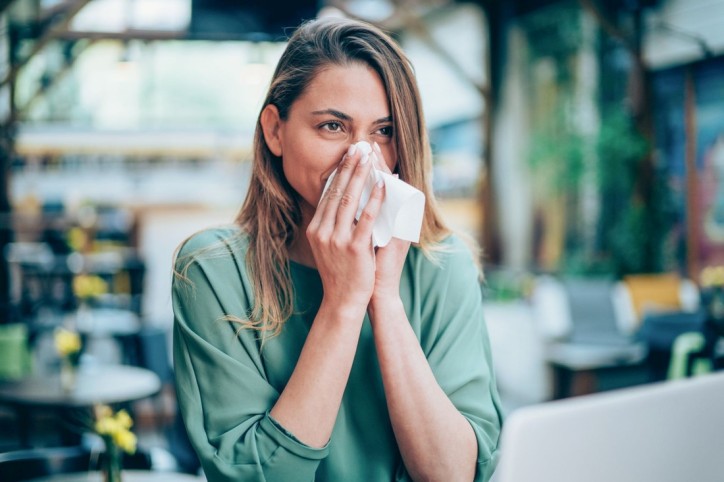 Eine Frau putzt sich aufgrund einer Pollenallergie die Nase.