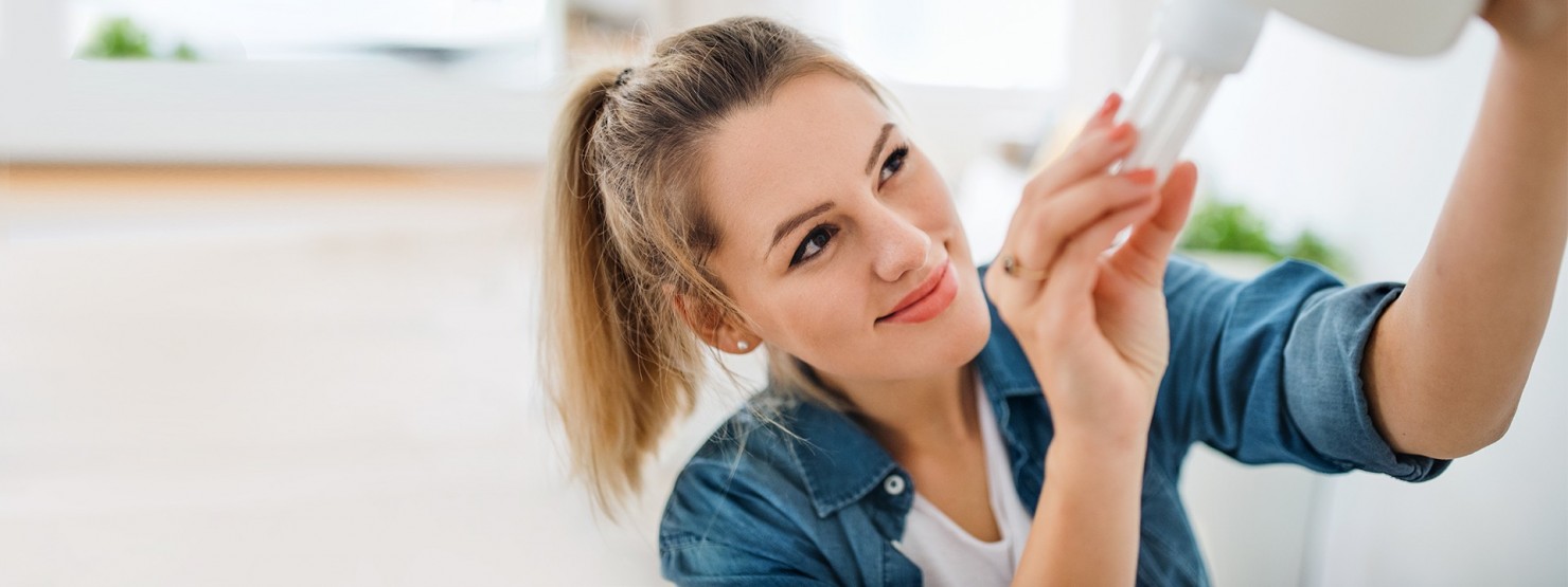 Eine etwa 30-jährige Frau schraubt eine Energiesparlampe in eine Fassung.