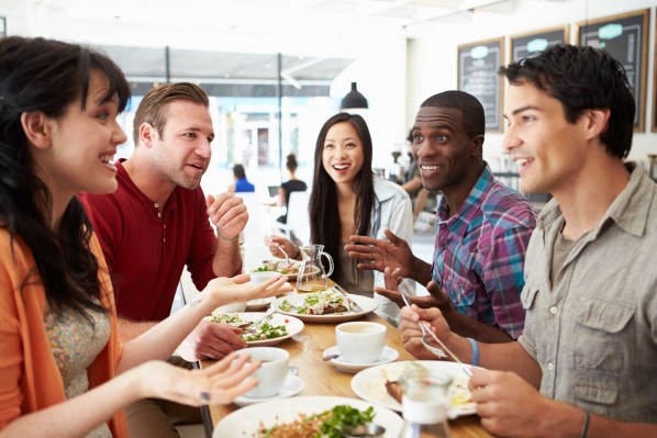 Eine fünf-köpfige Gruppe sitzt in einem Restaurant und isst und trinkt. dabei reden und lachen sie miteinander.