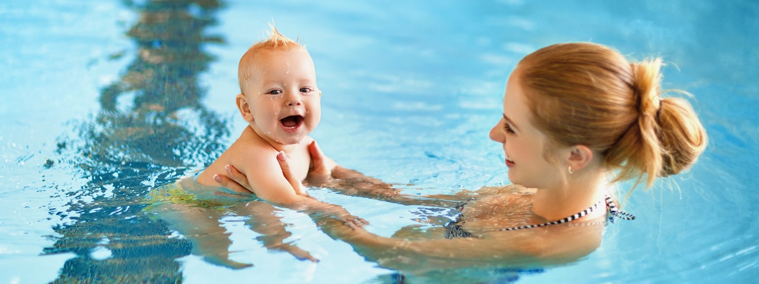 Mutter hält ihr Baby an den Händen und lässt es durch das Wasser gleiten
