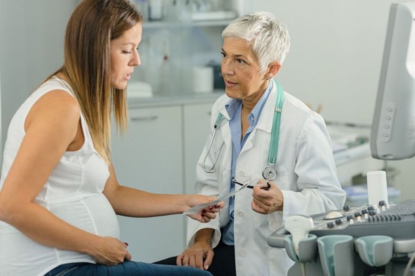 Schwangere Frau und ihre Ärztin in einer Konsultation. Frau hält Ultraschallbild und spricht mit der Ärztin.