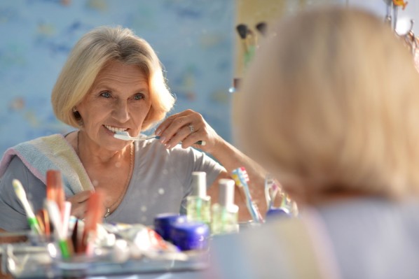 Eine etwa 60 jährige Frau steht vor dem Spiegel und putzt sich die Zähne.