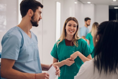 Eine Medizinstudentin spricht mit einer Patientin. Der Assistenzarzt beobachtet sie dabei.