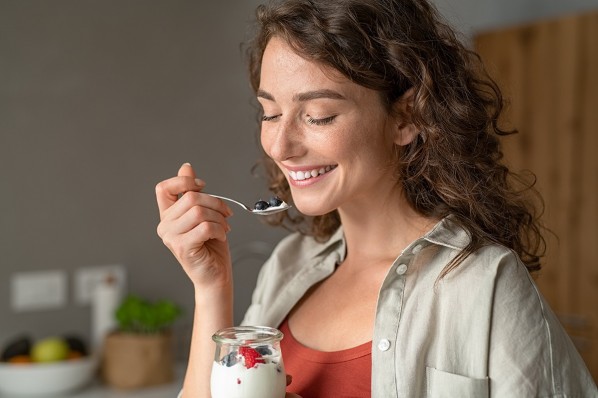 Eine etwa 30-jährige Frau isst Joghurt mit Beeren und lächelt.