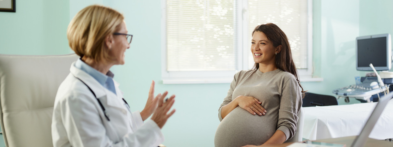 Glückliche schwangere Frau, die mit ihrem Gynäkologen im Büro spricht.