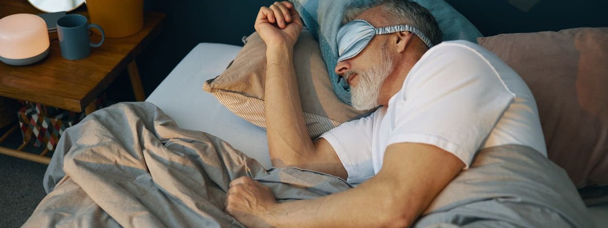 Älterer Mann mit Schlafmaske hält Schlafhygiene ein