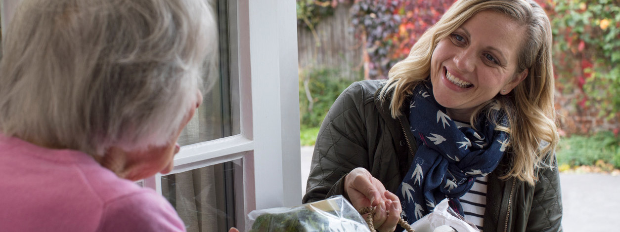 Eine Frau kümmert sich um die Einkäufe einer Seniorin