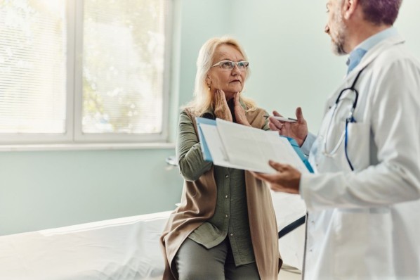 Eine Frau im Alter von 50 spricht mit ihrem etwa 60-jährigen Arzt über ihre Beschwerden in der Schilddrüse. 