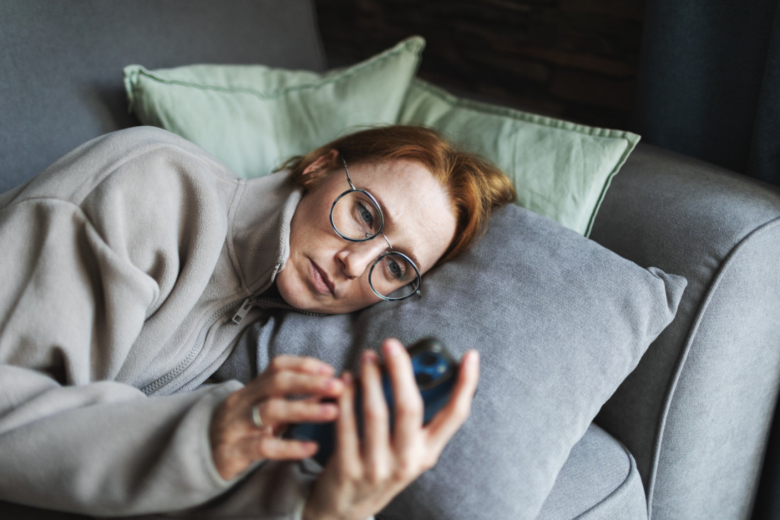 Junge Frau liegt erschöpft im bett und nutzt digitale medien