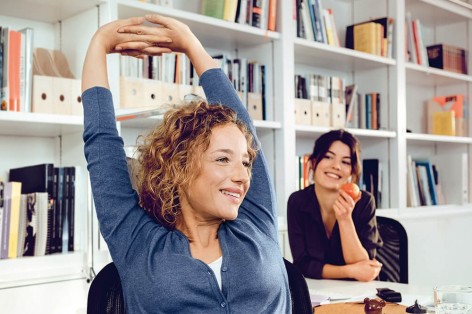 Eine Frau reckt am Schreibtisch Ihre Arme