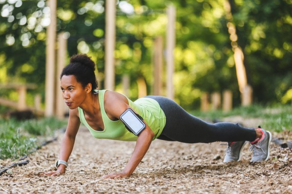 Frau beim Sport im Wald. Sie trägt Trainingskleidung und hat ihr Handy am Arm in einer Vorrichtung. 