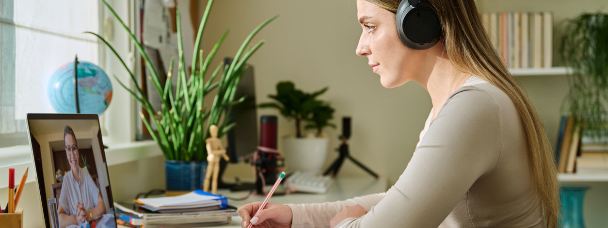 Eine junge Frau nimmt zuhause an einem medizinischem Online-Seminar teil und macht sich dabei Notizen.