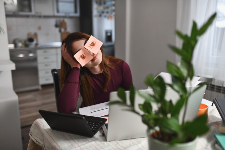 Eine Frau mit ADHS klebt sich Zettel ins Gesicht, anstatt ihre Arbeit zu erledigen