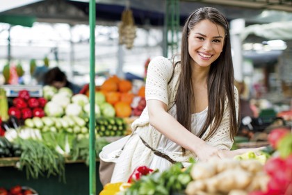 Brünette junge Frau kauft auf einem Markt Gemüse ein und lächelt.