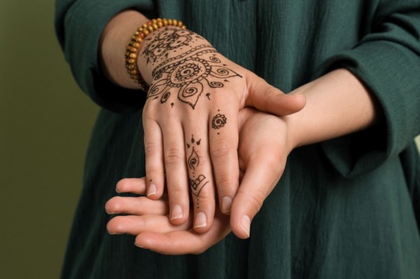Die Hände einer jungen Frau sind mit Henna-Tattoos verziert. Sie trägt ein dunkelgrünes Kleid. 