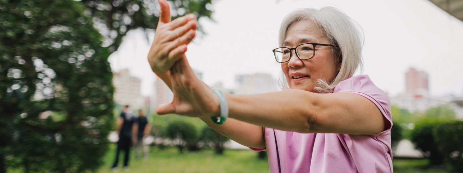 Eine etwa 70-jährige Frau praktiziert Tai-Chi im Park.