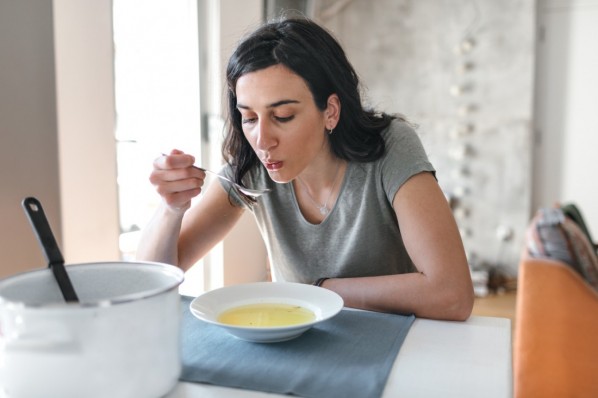 Frau Anfang 30 isst eine klare Suppe in ihrer Küche