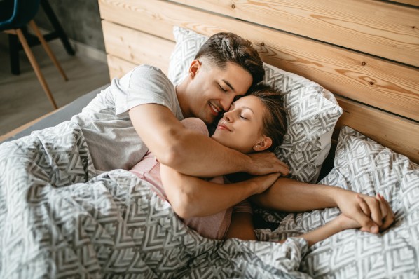 ein junges Paar mitte 20 liegt kuschelnd im bett