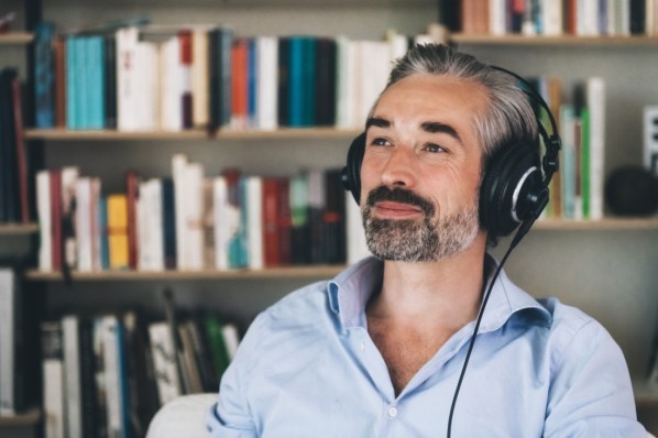 Mann Mitte 50 sitzt mit Noise-cancelling-Kopfhörern in seinem Büro