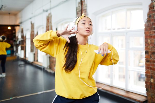 Eine etwa 25-jährige Frau tanzt mit Kopfhörern und Handy in der Hand Hiphop in einem Tanzstudio.