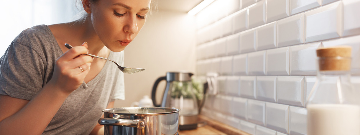 Eine Frau kostet mit einem Löffel auf einem Topf mit einem One-Pot-Gericht.